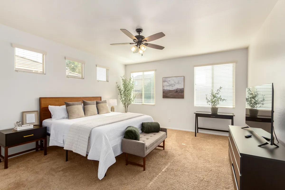 A serene bedroom featuring a comfortable bed, nightstand, dresser, and a leafy plant by the window. Sunlight pours in, creating a tranquil spot perfect for leisurely mornings or quiet evenings.