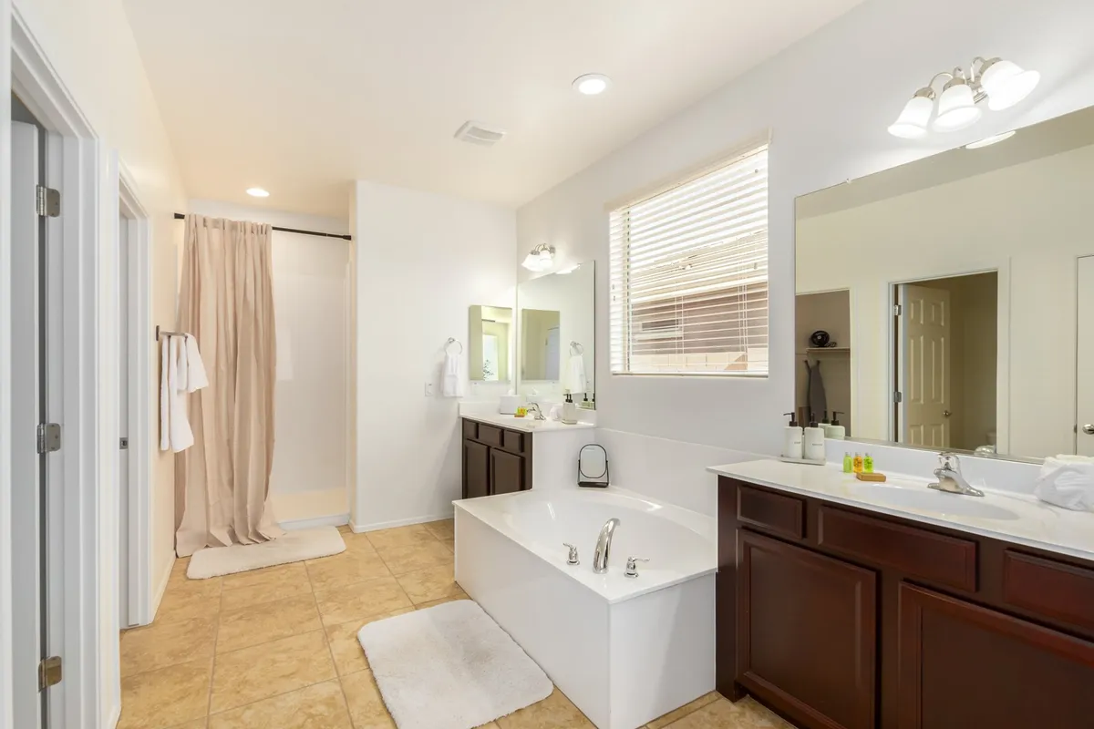 A modern bathroom with a spacious bathtub, mirrors, vanity, and glass shower area. The serene mood and soft lighting create an inviting environment for relaxation or shared routines.