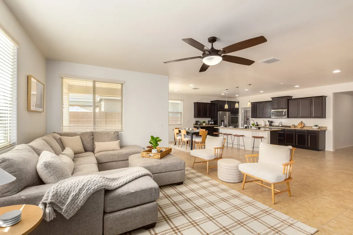A wide view of the open-concept main living area, seamlessly connecting the sectional sofa in the living room, an elegant dining table set for eight, and a kitchen island. Warm lighting and inviting decor create a cohesive, welcoming atmosphere.