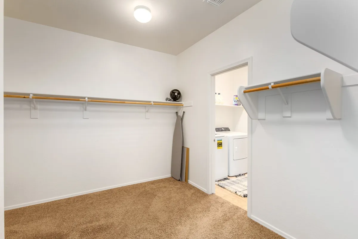 This image shows a bright, practical laundry room with a modern laundry machine, an ironing board, and storage shelves for organizing laundry essentials. The space is tidy and designed for efficient laundry routines.