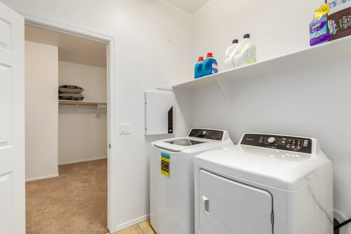 Neatly arranged shelves with detergent, a washing machine, a dryer, and a closet door evoke a sense of a clean, practical, and user-friendly laundry space. The setup highlights ample storage and organizational solutions for family needs.
