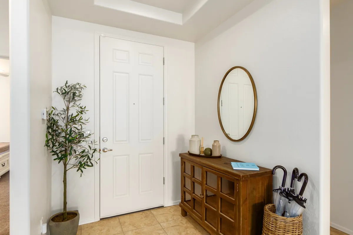 A welcoming view of the home's entryway, featuring the front door, mirror, wooden console table, and decorative plant. This space creates the first impression as you enter from outdoor activities, bridging the outside world and the home's inviting interior.