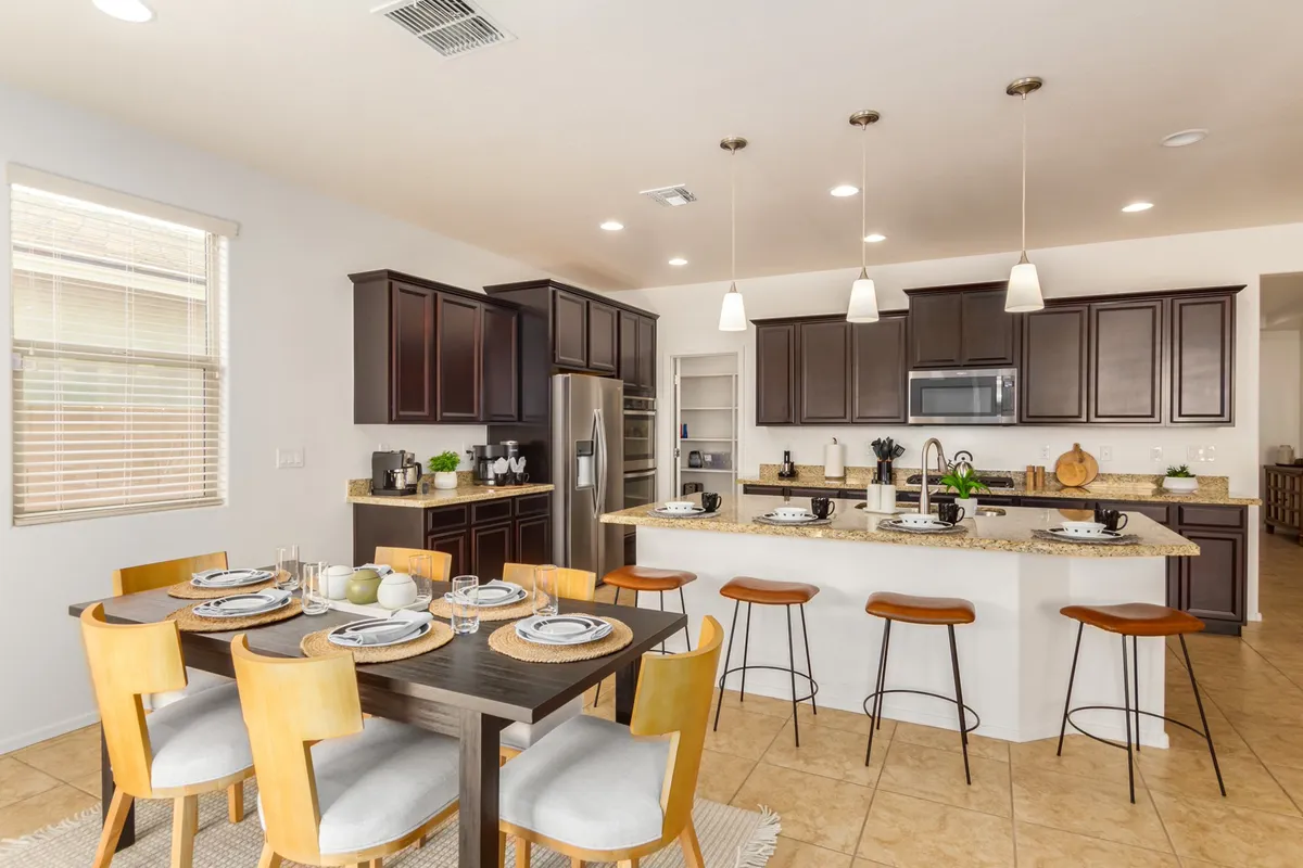A bright angle of the dining and kitchen space featuring a large dining table, kitchen island with bar stools, and modern cabinetry. The arrangement emphasizes shared meals and entertaining opportunities.